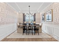 Elegant dining room featuring wainscoting, patterned wallpaper, and modern chandelier over a wood table at 1471 Hubert Graham Way, Tega Cay, SC 29708