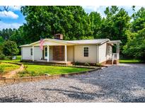Charming single-story home with an inviting front porch, American flag, and gravel driveway at 7050 Forney Hill Rd, Denver, NC 28037