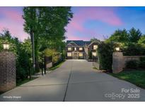 Elegant home with gated entrance, long driveway, and manicured landscaping visible at dusk at 7944 Park Rd, Charlotte, NC 28210