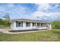 Charming, white, single-story home with dark shutters, wood porch, and well-maintained lawn at 6599 Mcintosh Rd, Stanley, NC 28164