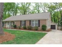 Charming brick home with manicured lawn, brown shutters, and a detached garage in a peaceful, wooded setting at 7626 Surreywood Pl, Charlotte, NC 28270