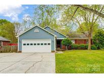Charming single-story home with a blue exterior, well-manicured lawn, and attached two car garage at 13417 Krislyn Woods Pl, Charlotte, NC 28278