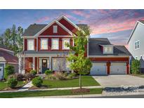 Charming two-story home with red siding, a three-car garage, and a beautifully landscaped front yard at 2329 Paddlers Cove Dr, Clover, SC 29710