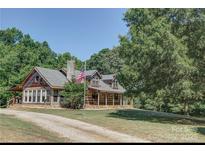 Charming log cabin home featuring a lush lawn, American flag, and a long private driveway at 3014 Haigler Rd, Monroe, NC 28110