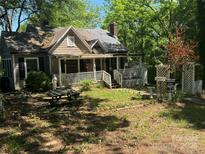 Exterior front view of a home with a porch, weathered finishes, and a partially overgrown front yard with foliage at 902 W 6Th Ave, Gastonia, NC 28052