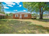 Charming brick home features a well-maintained lawn, fenced yard, and a small wooden deck perfect for enjoying the outdoors at 3203 Valleydale Rd, Monroe, NC 28110