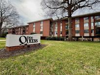 Brick condo building with '1300 Queens' sign, lawn, and mature trees creating a welcoming exterior view at 1300 Queens Rd # 210, Charlotte, NC 28207