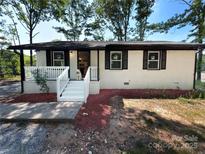 Charming home with a white brick facade, black shutters, and a welcoming front porch and a cute white dog at 1407 Clarksville Campground Rd, Monroe, NC 28112