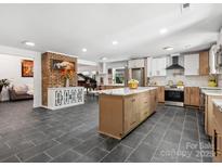 Spacious kitchen with gray tile floors, brick accent wall, island, white cabinets and stainless steel appliances at 6724 Brushwood Dr, Charlotte, NC 28262