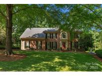 Traditional brick home featuring a manicured lawn, mature trees, black shutters, and a welcoming red front door at 6017 Summerston Pl, Charlotte, NC 28277