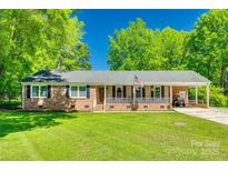Charming single-story brick home featuring a covered front porch, well-manicured lawn, and mature trees at 1938 Hickory Dr, Lancaster, SC 29720