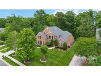Aerial view of a brick home with a well-manicured lawn, mature trees, and black shutters on a sunny day at 7302 Yellowhorn Trl, Waxhaw, NC 28173