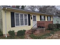 Charming yellow home features a brick foundation, black shutters, and a landscaped yard at 828 Williams St, Gastonia, NC 28052