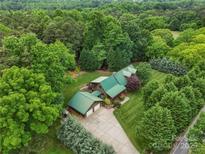 Stunning aerial view of a green-roofed log home nestled within a lush, dense forest at 10583 Earnhardt Lake Rd, Davidson, NC 28036