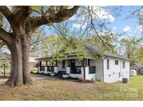 A charming white house is nestled beneath a tree with fresh landscaping and a inviting porch at 221 Palmer St, Albemarle, NC 28001