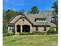 Charming brick home featuring a manicured lawn, arched porch, and classic architectural details on a sunny day at 15210 Pavilion Valley Cir, Huntersville, NC 28078