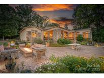 Inviting outdoor space with stone patio, fire pit, seating, and lush landscaping at sunset at 542 Lochaven Rd, Waxhaw, NC 28173
