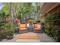 Relaxing patio with orange cushioned seating, potted plants, and beautiful green surroundings at 7444 Hurstbourne Green Dr, Charlotte, NC 28277