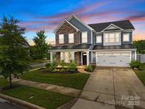 Charming two-story home showcasing stone accents, blue siding, lush landscaping, and a two-car garage at 12710 Es Draper Dr, Huntersville, NC 28078