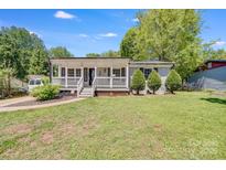 Charming home featuring a covered front porch, manicured lawn, and gray brick exterior at 2614 Thornton Rd, Charlotte, NC 28208