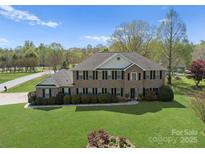 Stately brick home featuring mature landscaping and a large, manicured lawn under a blue sky at 1052 Perth Rd, Troutman, NC 28166