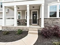 Charming front porch with stone accents, white pillars, and a welcoming entrance. Seating for two at 10035 Mast Cove Ln, Charlotte, NC 28278