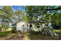 Cozy single story home with white siding and a small porch surrounded by lush greenery and flowers at 2118 Polkville Rd, Shelby, NC 28150