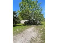 Tan single-story home featuring a gravel driveway, lush lawn, and mature trees at 104 Poplar St, Clover, SC 29710