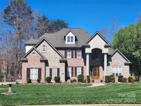 Elegant two-story brick home with stone accents, arched entry, and lush, manicured lawn under a clear blue sky at 6927 Ellington Farm Ln, Mint Hill, NC 28227