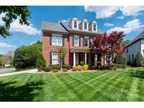 Beautiful brick home featuring a lush front lawn, mature trees, and classic architectural details at 12122 Camden Trail Ct, Charlotte, NC 28277