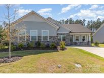 Charming single-story home featuring stone accents, light blue siding, well-manicured lawn and inviting front porch with rocking chairs at 8011 Green Heron Ct, Belmont, NC 28012