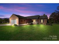 Charming brick home featuring manicured lawn, attached two-car garage, and welcoming front porch under a beautiful sunset at 131 Fieldhaven Pl, Troutman, NC 28166