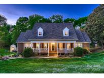 Inviting brick home featuring a covered front porch, dormer windows, and lush green lawn at 308 Valhalla Dr, Harrisburg, NC 28075
