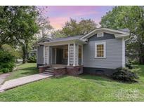 Charming home with a welcoming front porch, gray siding, and manicured lawn with a brick walkway and foundation at 303 S Iredell Ave, Spencer, NC 28159