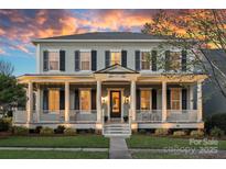 Charming two-story home featuring a covered front porch with stately columns and beautiful landscaping at sunset at 9803 Tree Canopy Rd, Charlotte, NC 28277