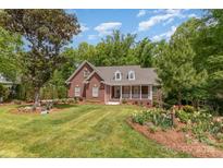 Brick home featuring a manicured lawn and front porch nestled amongst mature trees at 5283 Fieldstone Dr, Concord, NC 28025