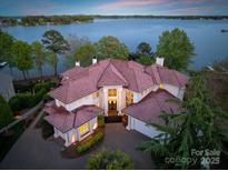 Expansive lakefront home features a red tile roof, manicured landscaping, and a circular driveway at 102 Eastham Ct, Mooresville, NC 28117