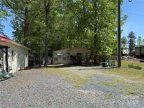 Exterior view of home with gravel parking and carport surrounded by mature trees, offering shade and privacy at 104 Powder Horn Trl # C92, Mount Gilead, NC 27306