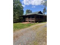Charming cabin-style home with a large covered porch and gravel driveway surrounded by lush greenery and trees at 9751 Quail Run Rd, Locust, NC 28097