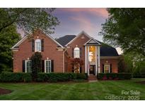 Beautiful red brick home with a manicured lawn and a two-story entrance with white pillars at dusk at 9217 Rock Water Ct, Waxhaw, NC 28173