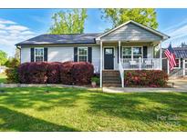 Charming home with a well-manicured lawn and a cozy front porch decorated with flowering bushes and an American flag at 303 Caroline Ave, Lowell, NC 28098