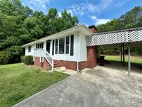 Charming single-story home with white siding, brick accents, and a covered carport, surrounded by lush greenery at 12719 Cottonville Rd, Norwood, NC 28128