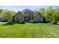 Charming stone facade home featuring mature trees, lush landscaping, and a well-manicured lawn at 15909 Heath Aster Way, Davidson, NC 28036