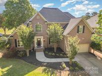 Stunning brick two-story home with well-manicured lawn and mature trees, with a driveway leading to a two-car garage at 12004 Willingdon Rd, Huntersville, NC 28078