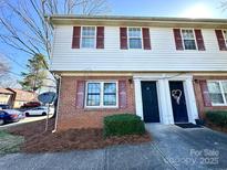 Charming two-story townhome featuring red brick and vinyl siding, complemented by red shutters and landscaped entrance at 5812 Hunting Ridge Ln # A, Charlotte, NC 28212