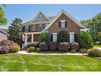 Charming brick home with a covered front porch, lush landscaping, and a well-manicured lawn at 10716 Persimmon Creek Dr, Mint Hill, NC 28227