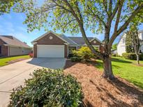 Charming brick home featuring a two-car garage and a beautifully landscaped front yard with mature trees on a sunny day at 4656 Chaucer Nw Pl, Concord, NC 28027