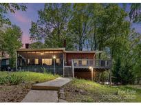 Charming lake house featuring a screened porch and deck overlooking a lush, wooded lot at dusk at 1278 Island Creek Dr, Troy, NC 27371