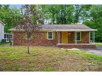 Charming brick home with a covered porch, yellow front door, green shutters, and mature landscaping at 6558 Covecreek Dr, Charlotte, NC 28215