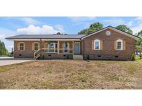 Charming brick ranch featuring a metal roof, wooden window shutters, and an inviting covered porch at 124 Hunters Creek Dr, Mooresville, NC 28115